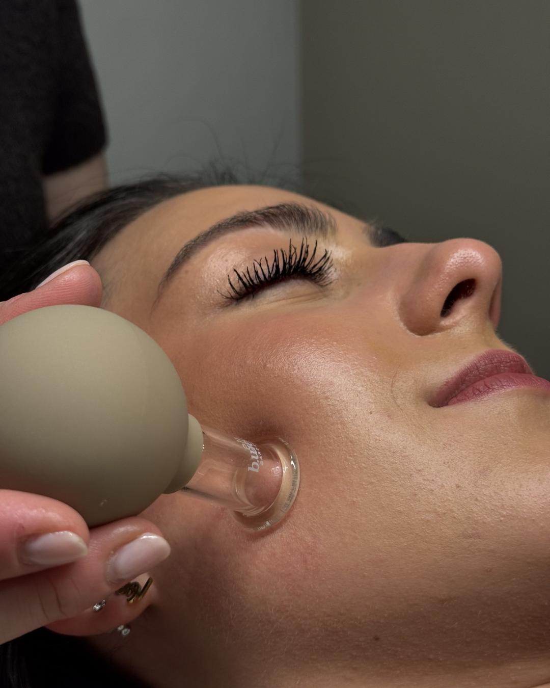 Face-Pilates-Behandlung mit Schröpfglas an Wange und Kiefer